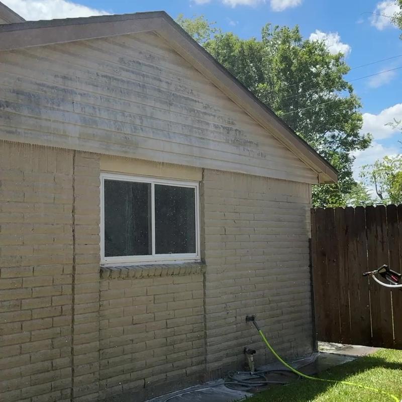Tan brick wall and siding gable, wet, with darker streaks still visible on the gable